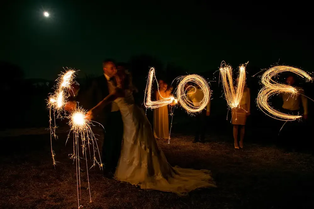 Mariés et invités dessinant le mot « LOVE » avec des cierges magiques pendant une soirée de mariage.