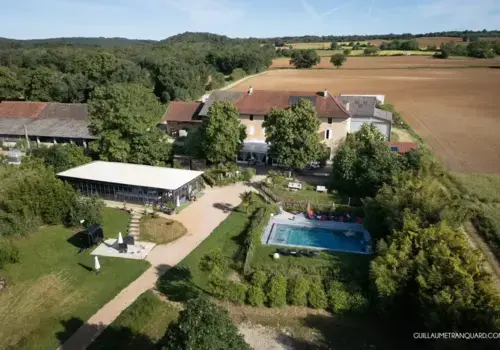 Vue aérienne du Domaine des Plagnes avec bâtisse en pierre, tente de réception, piscine, champs et verdure.