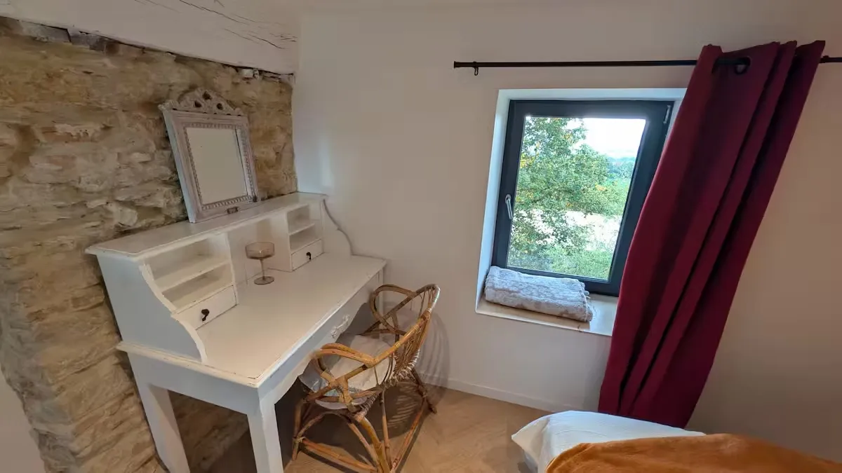 Chambre avec coiffeuse blanche ancienne, mur en pierre apparente et vue sur la verdure