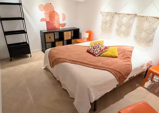Chambre avec lit double, couverture terracotta, macramé mural et fresque florale