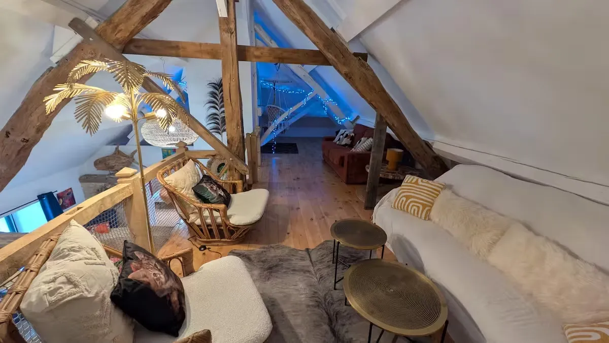 Mezzanine du gîte avec poutres sablées, chaises suspendues et guirlandes lumineuses