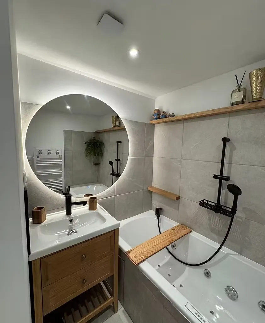 Salle de bain avec baignoire balnéo, miroir rond rétroéclairé et vanité en bois