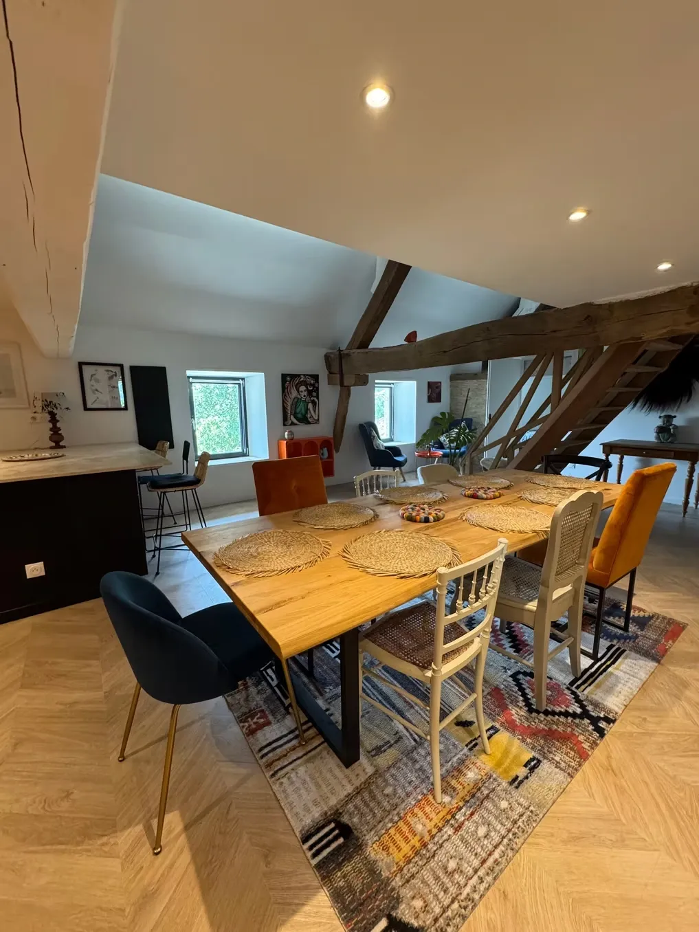 Grande salle à manger avec table en bois massif, chaises dépareillées et poutres sablées