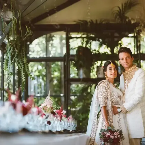 Couple de mariés posant dans l'Orangerie devant une table décorée de fleurs