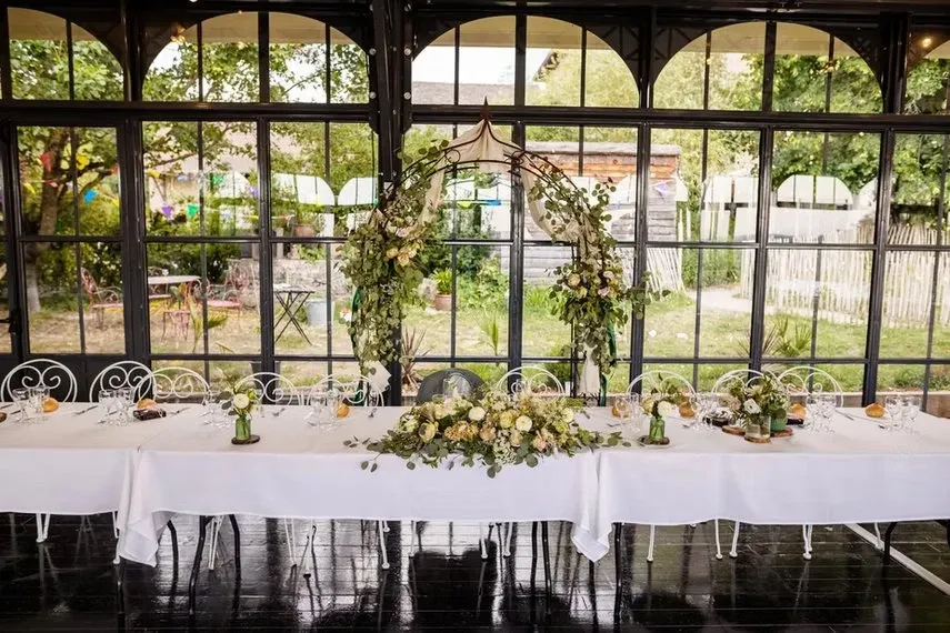 Table d'honneur dans l'Orangerie avec arche florale en eucalyptus et roses blanches