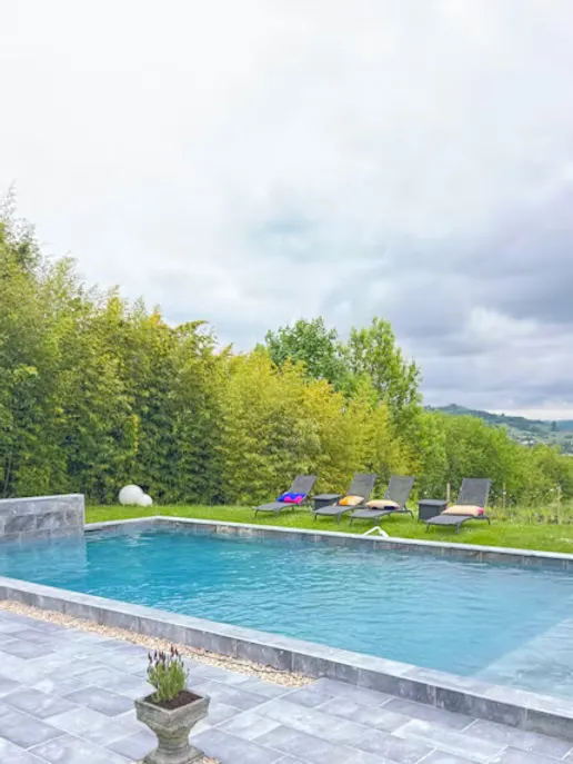 Piscine extérieure et terrasse en pierre du Domaine des Plagnes, avec transats et jardin arboré