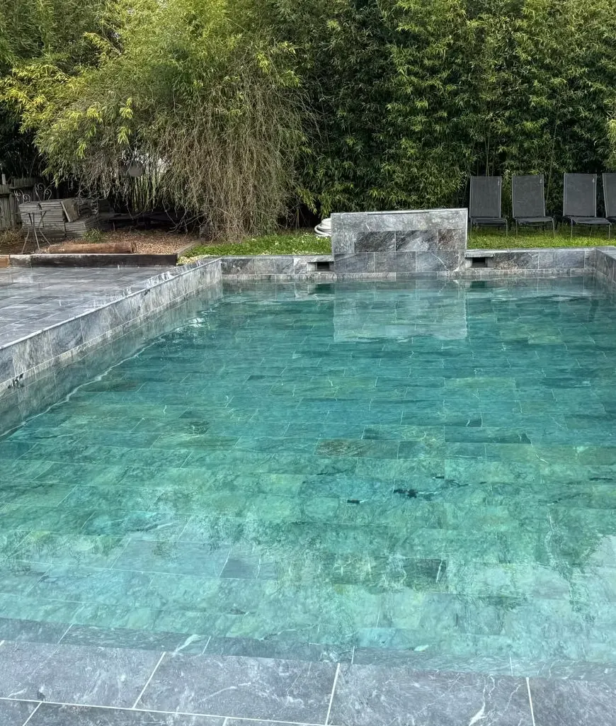 Piscine extérieure en pierre grise du Domaine des Plagnes, entourée de transats et de végétation.