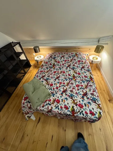 Chambre avec lit fleuri motif oiseaux exotiques et parquet bois brut