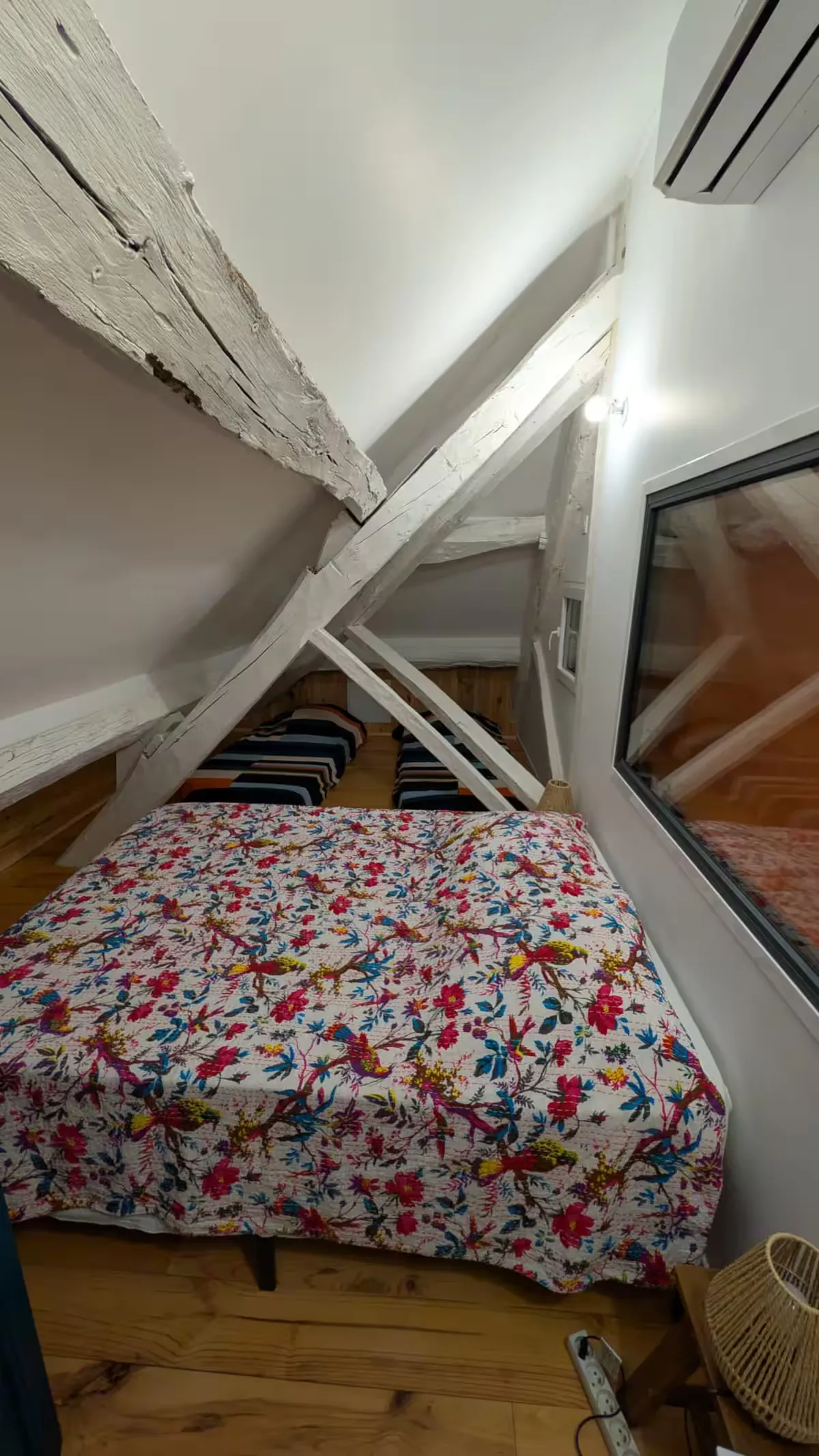 Chambre mansardée avec lit fleuri, poutres blanches et climatisation