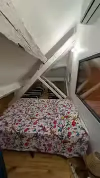 Chambre mansardée d’un gîte du Domaine des Plagnes avec lit fleuri, poutres blanches et climatisation.