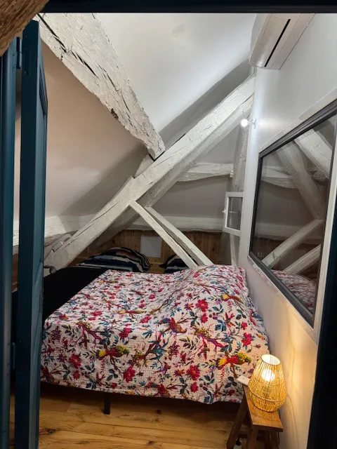 Chambre mansardée avec lit fleuri, poutres blanches et fenêtre de toit