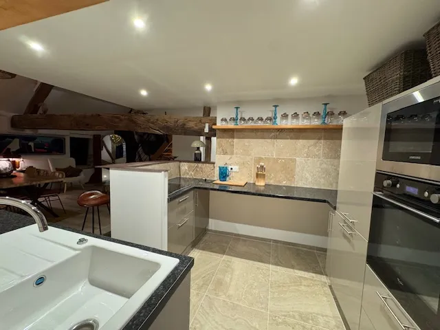 Cuisine équipée sous les combles avec mobilier blanc, plans gris et fours encastrés