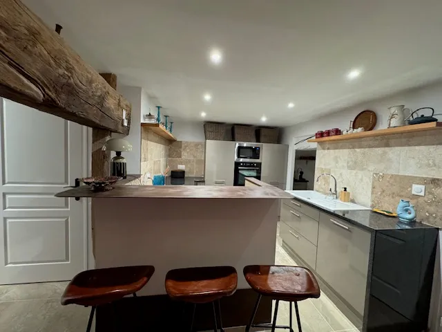 Cuisine moderne avec bar et tabourets bois, carrelage travertin et poutres