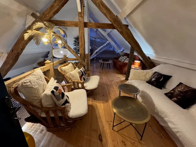 Mezzanine du Gîte Les Tilleuls avec poutres apparentes, fauteuils en rotin et canapé blanc