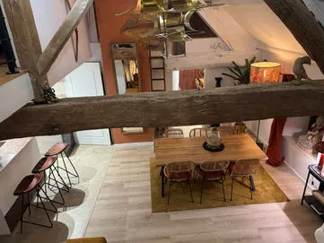 Salle à manger et cuisine ouverte d'un gîte du Domaine des Plagnes vues depuis la mezzanine, avec poutres anciennes.