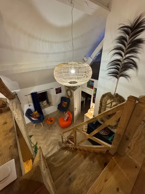 Vue plongeante depuis la mezzanine sur le salon — suspension rotin, escalier bois et décoration boho